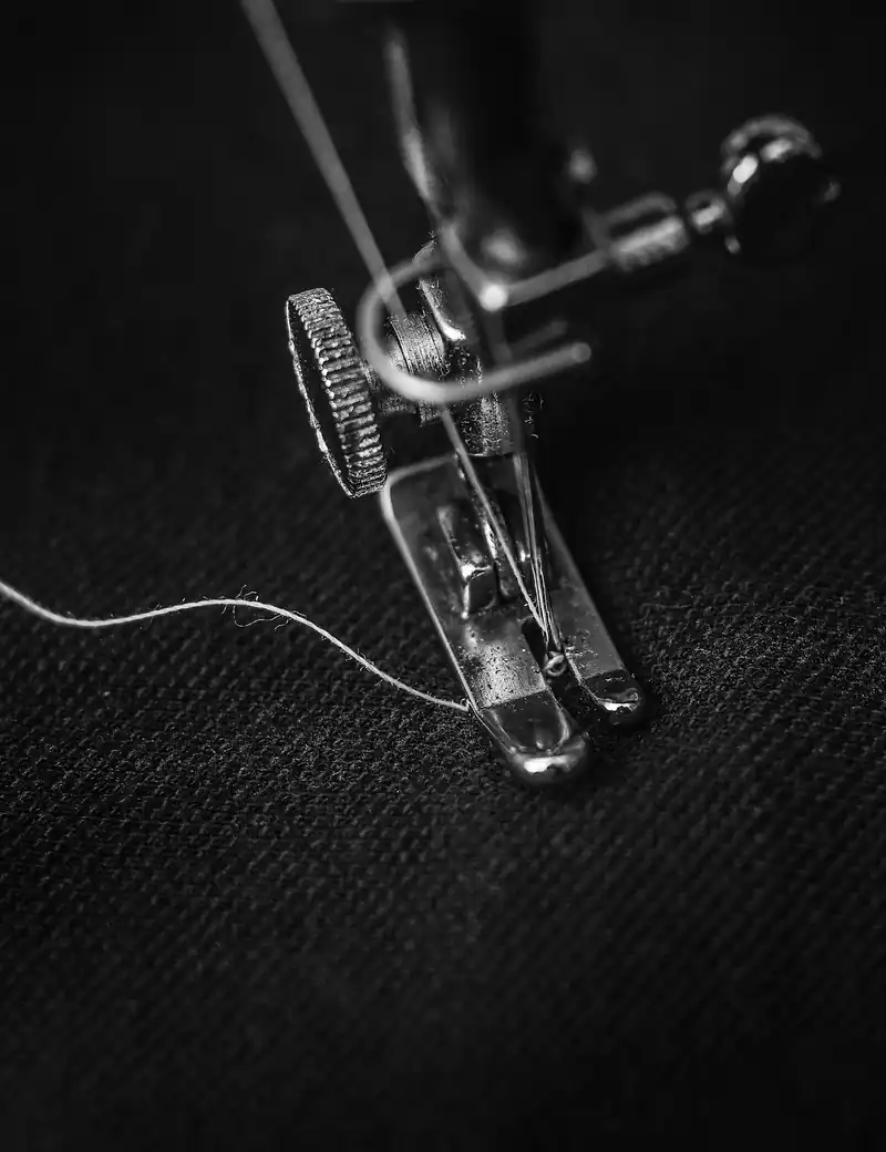 A sewing machine needle and presser foot stitching dark fabric